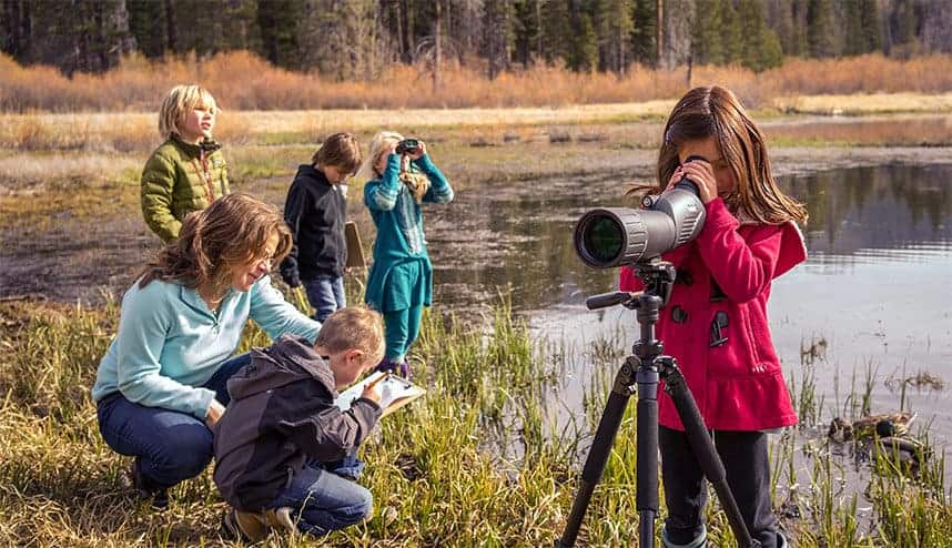 student looks through a telescope by a lake
