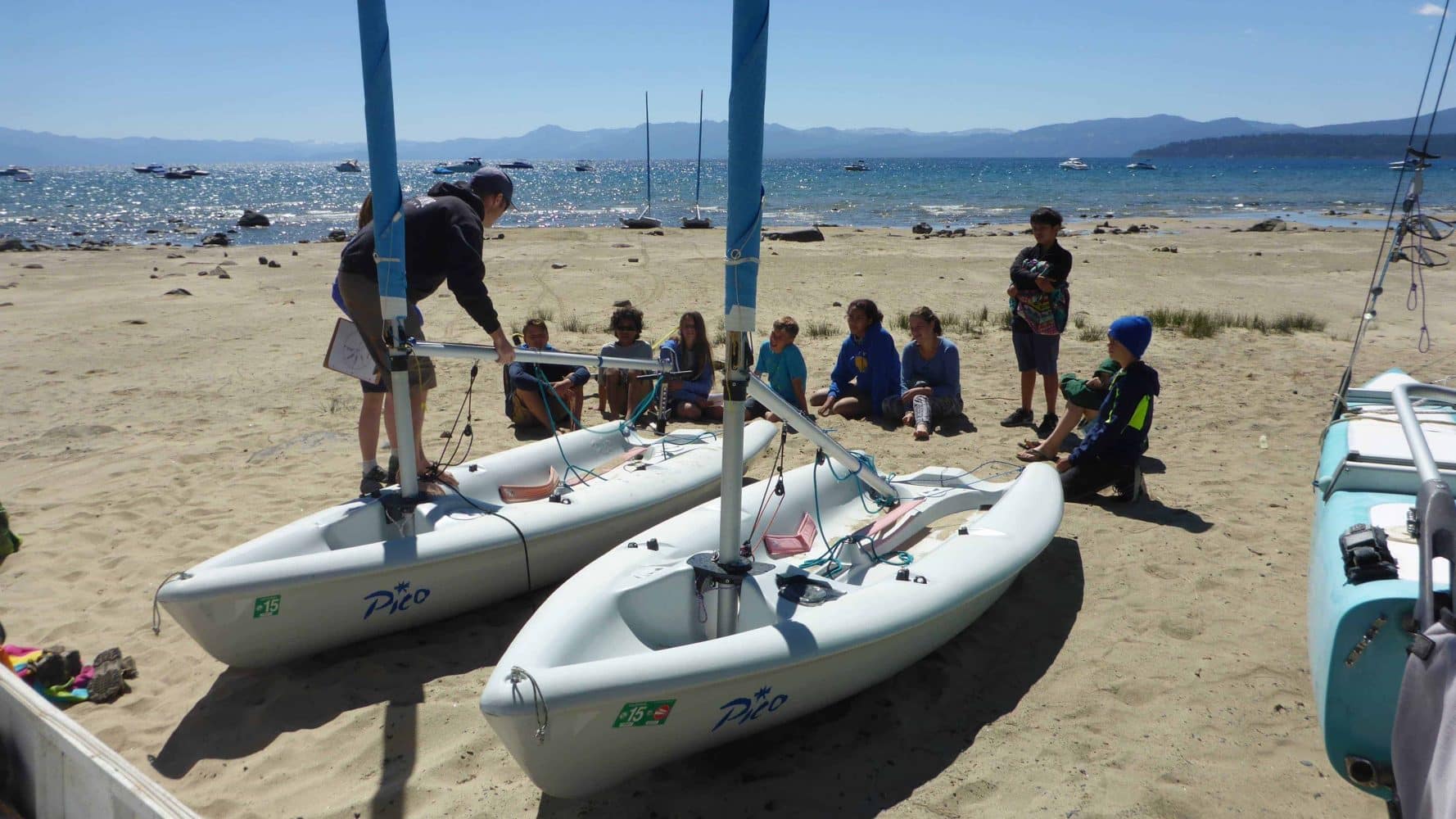 students on shore with their sailboats