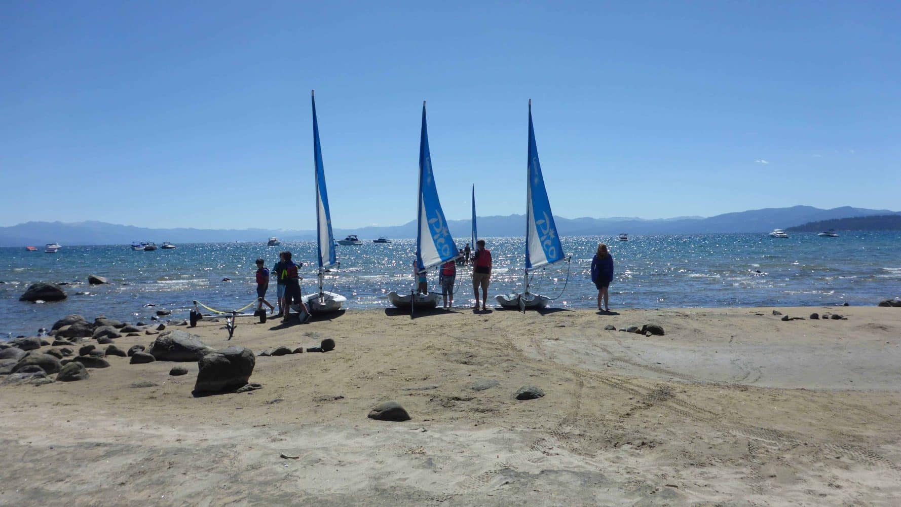 students on shore with their sailboats