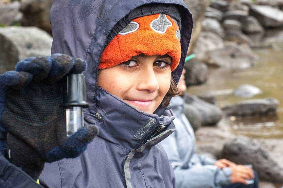 student in hat and jacket holding a water sample