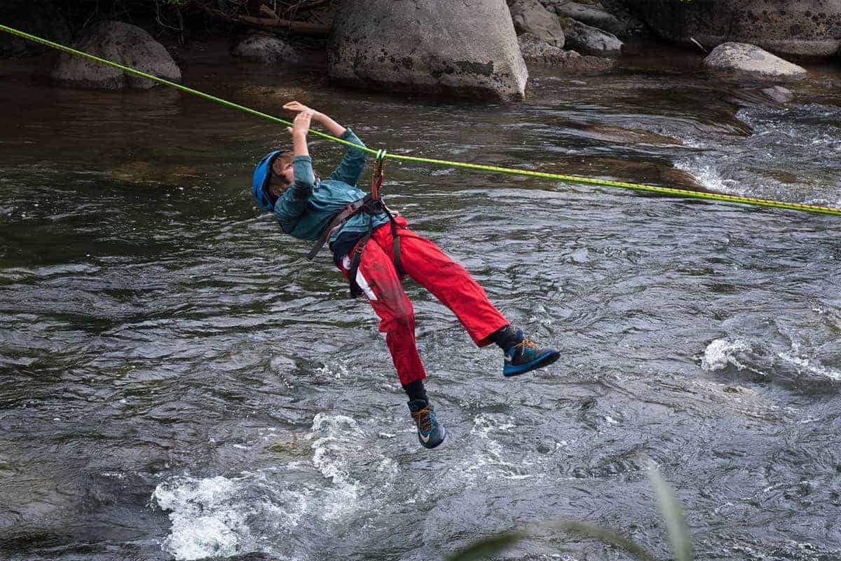 student in a rope harness over a river