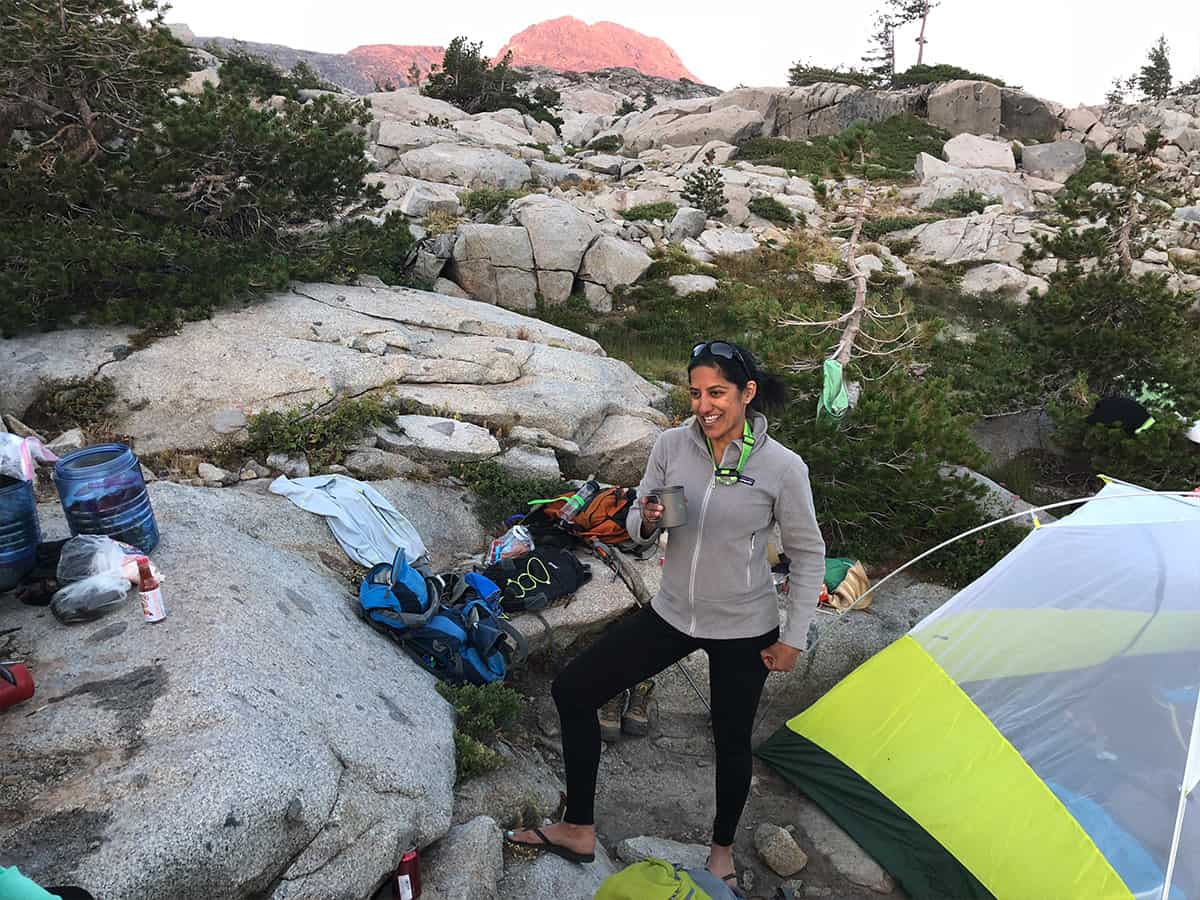 a backpacking crew member next to a tent smiling for the camera