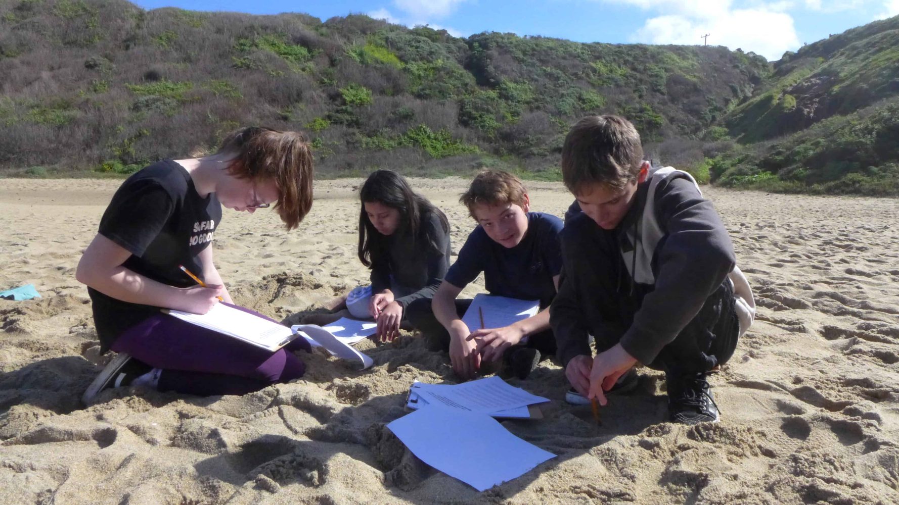 students sitting in the sand taking notes