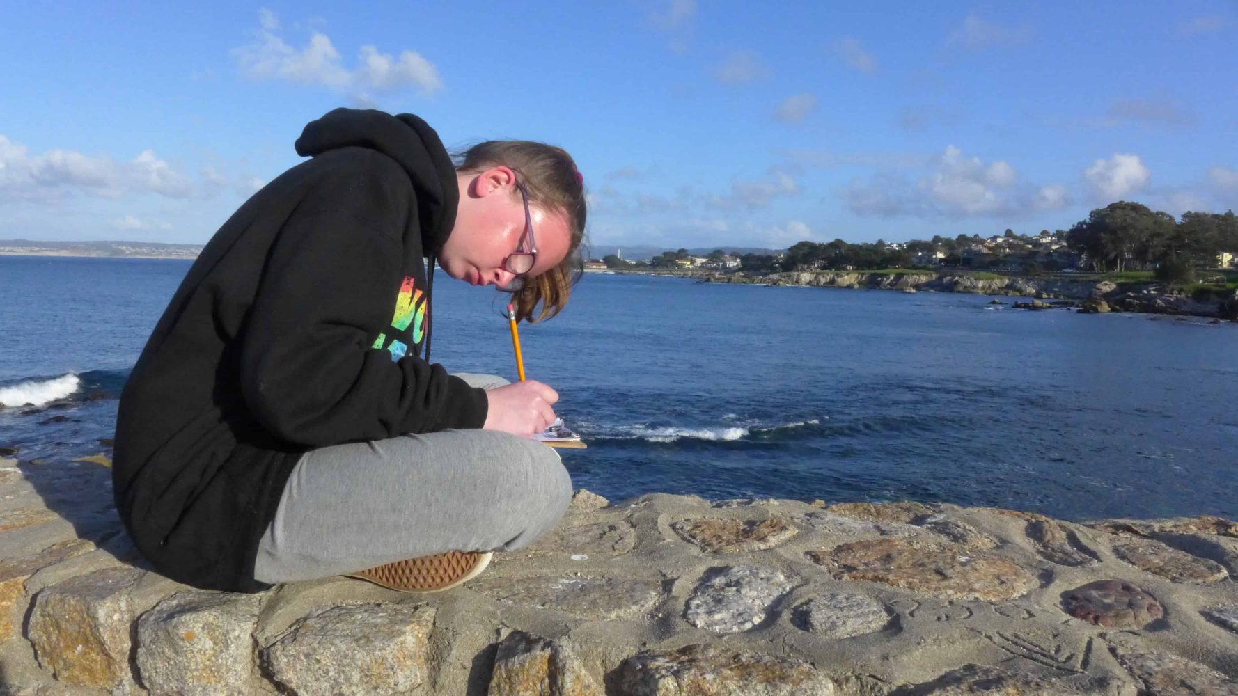 a boy sitting on a rock next to the beach