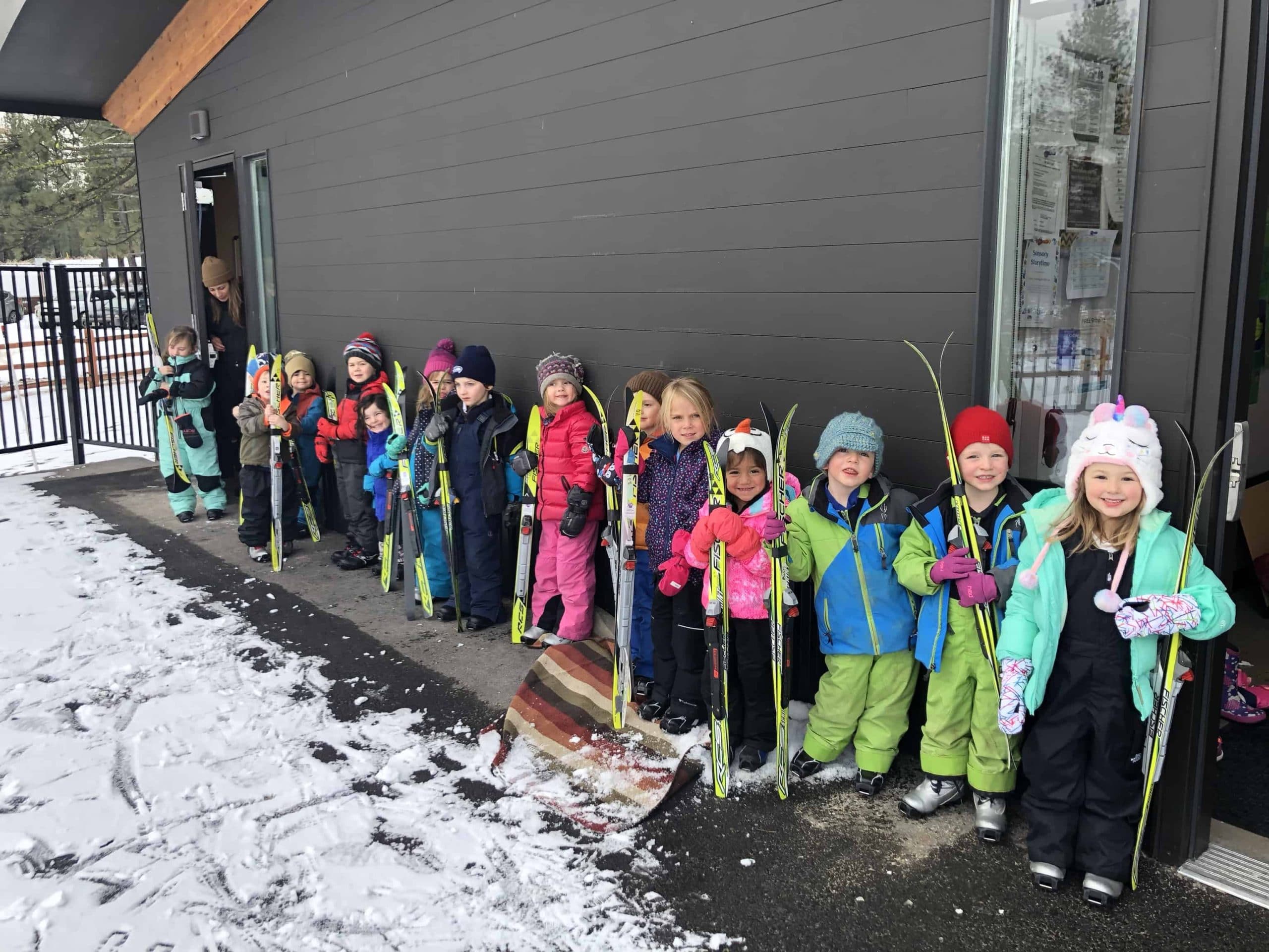 kids line up against the wall with their skis in hand