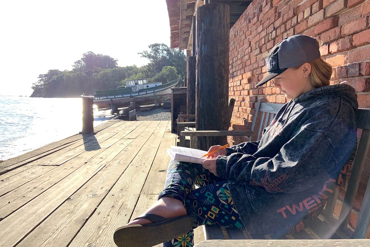a kid at a pier studying on a bench