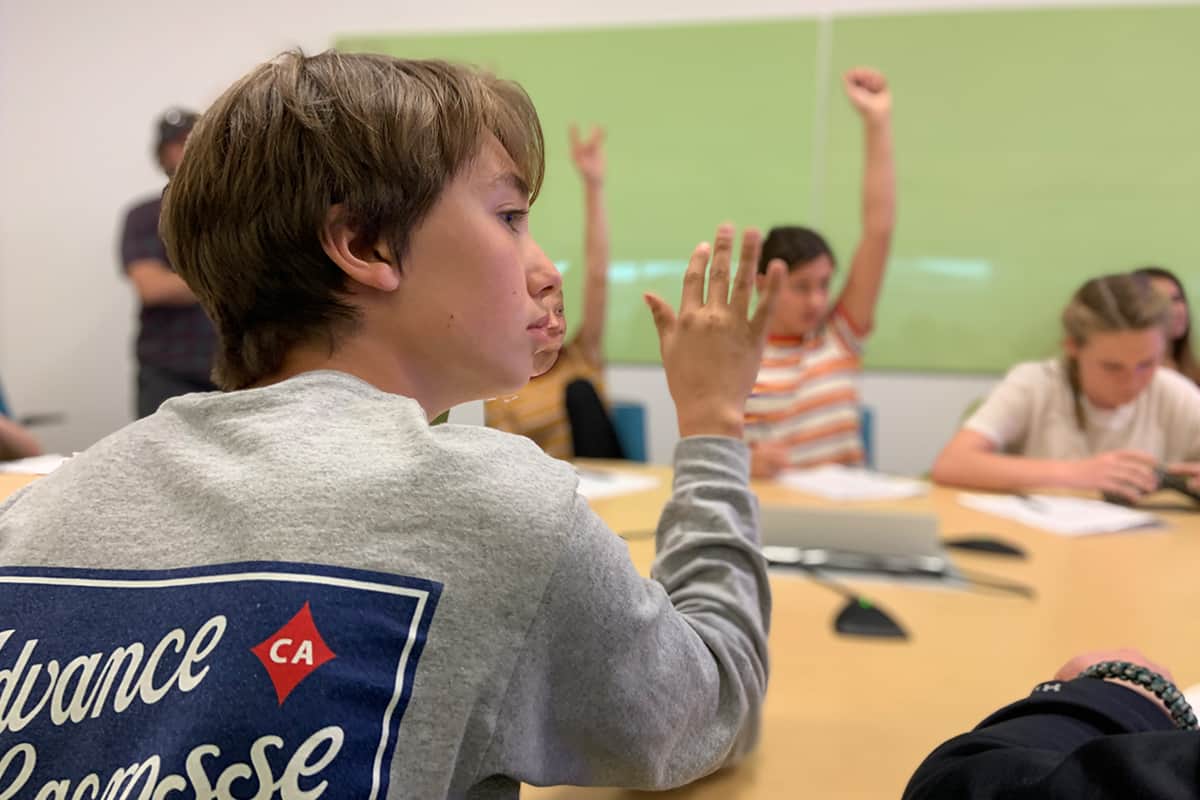 kids sitting at a desk raising their hands